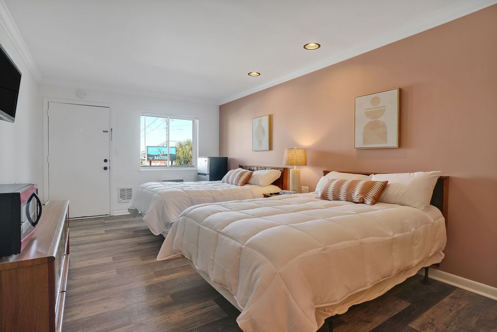 A hotel room with two beds, a television, a desk, and a window with a view of the outside.