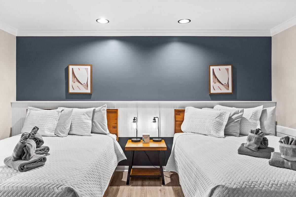 A hotel room with two beds, a nightstand, and two framed pictures on the wall.