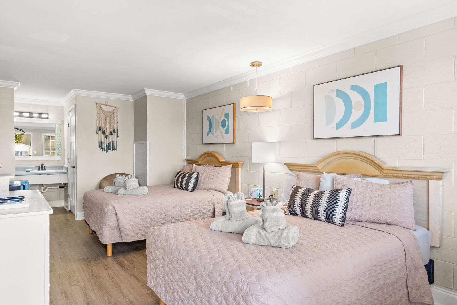 Una habitación de hotel con dos camas, una zona de estar con escritorio y obras de arte en las paredes.