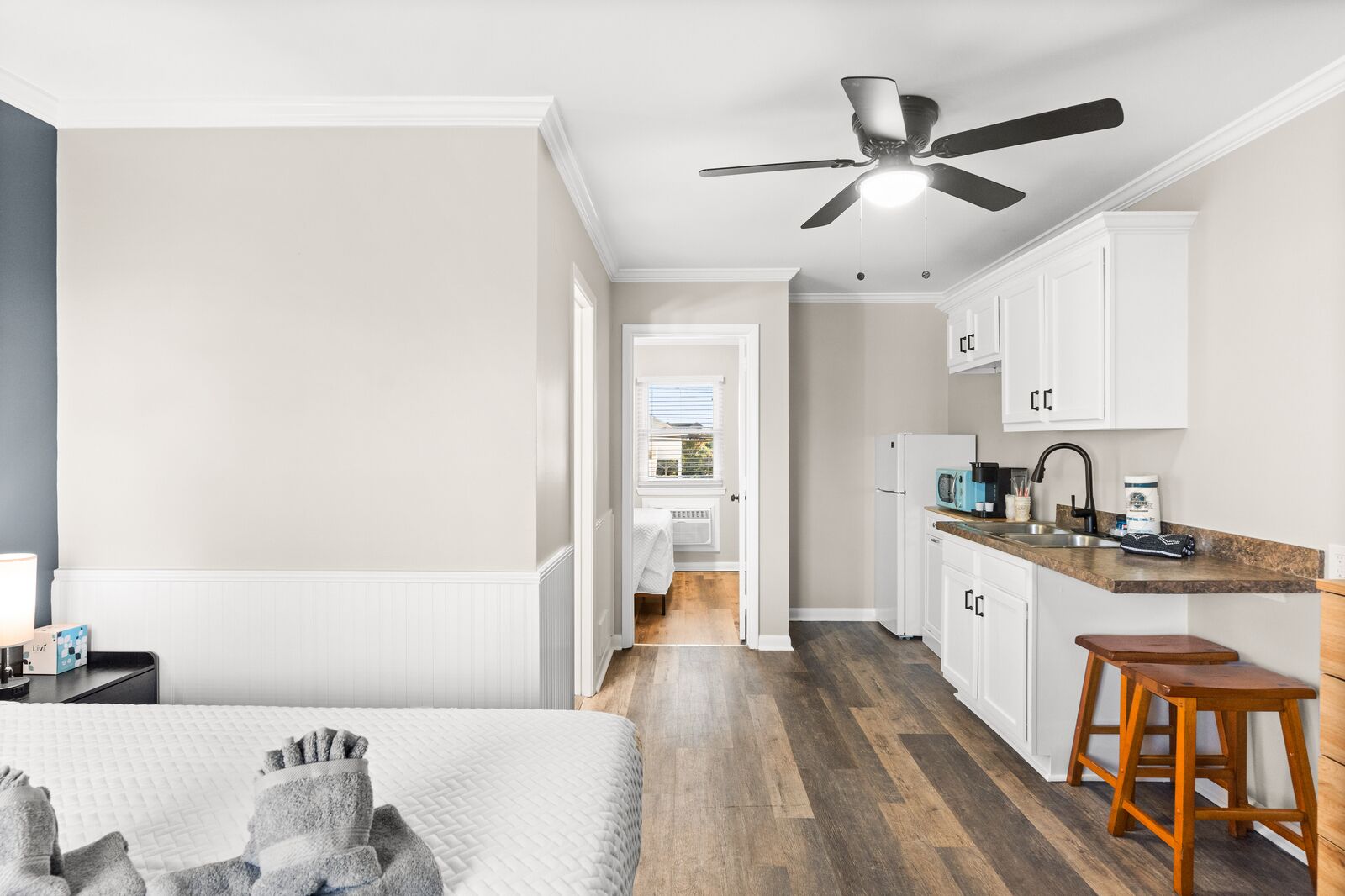 A modern, well-lit room with a bed, a desk, and a kitchenette.