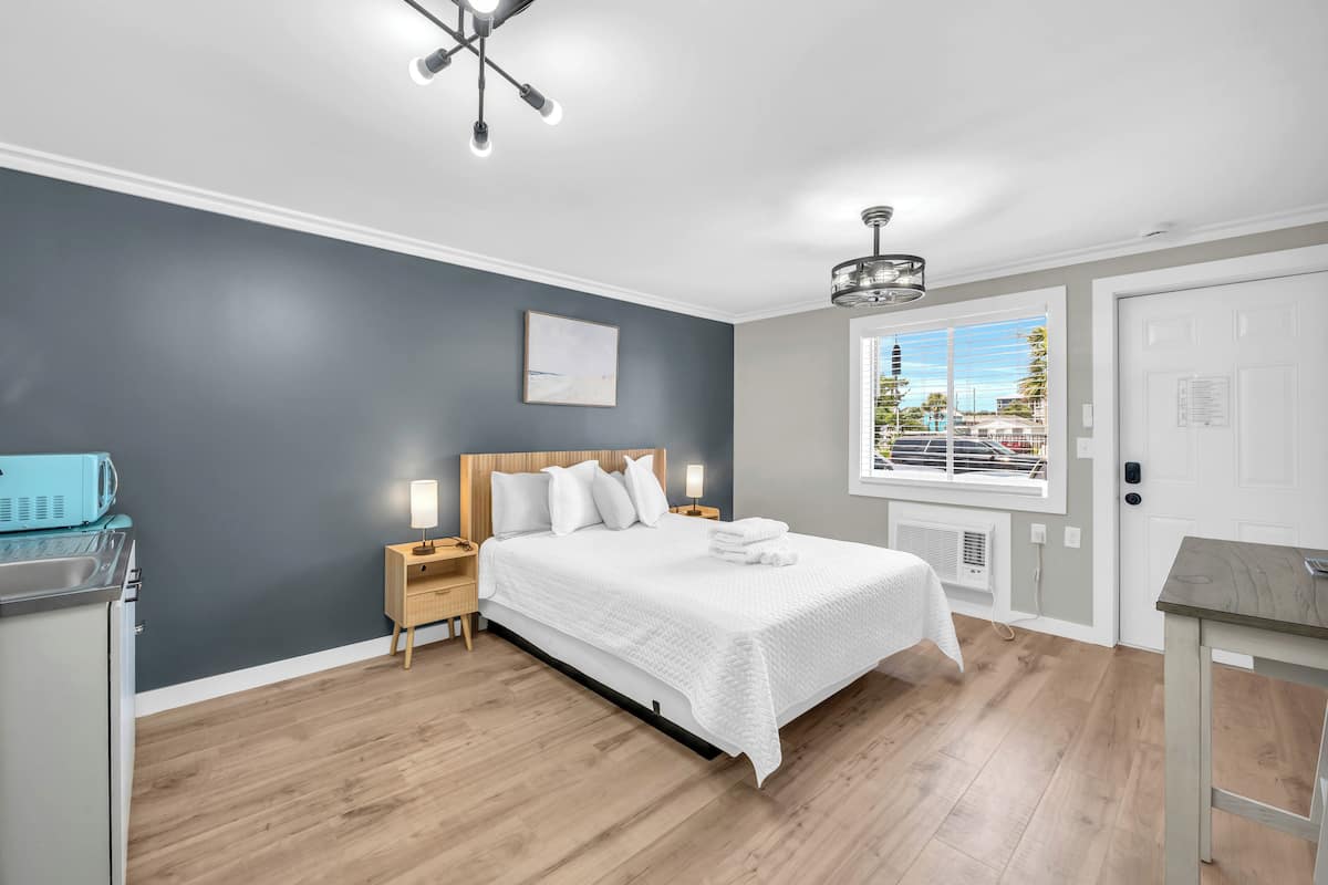 A modern bedroom with a large bed, wooden headboard, bedside lamps, and a view of the outdoors through a window.