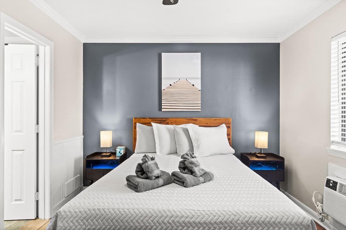 A neatly arranged bedroom with a large bed, two bedside tables with lamps, a wall-mounted artwork, and a radiator.