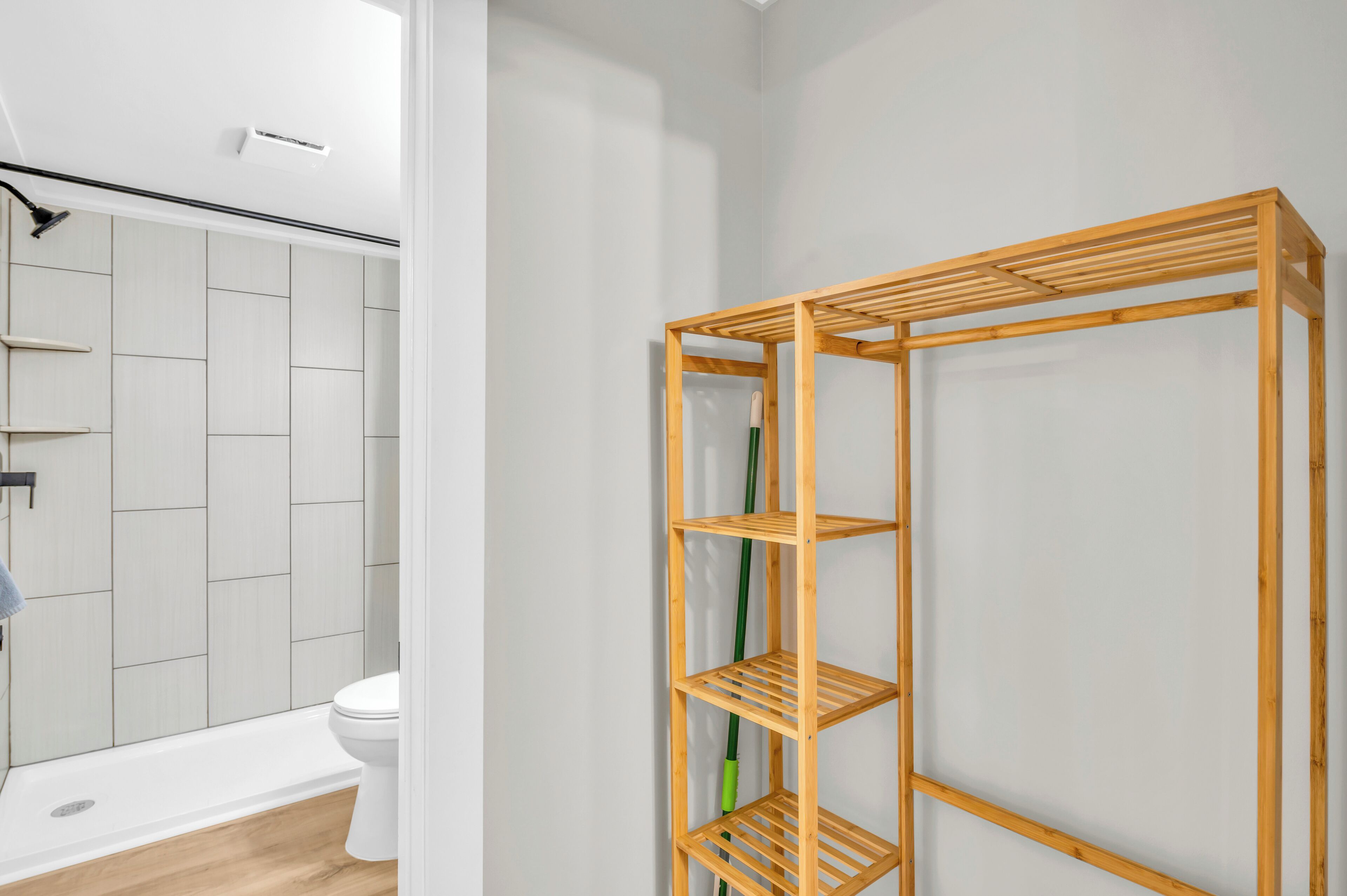 A bathroom with a white toilet, a wooden shelf unit, and a shower area.