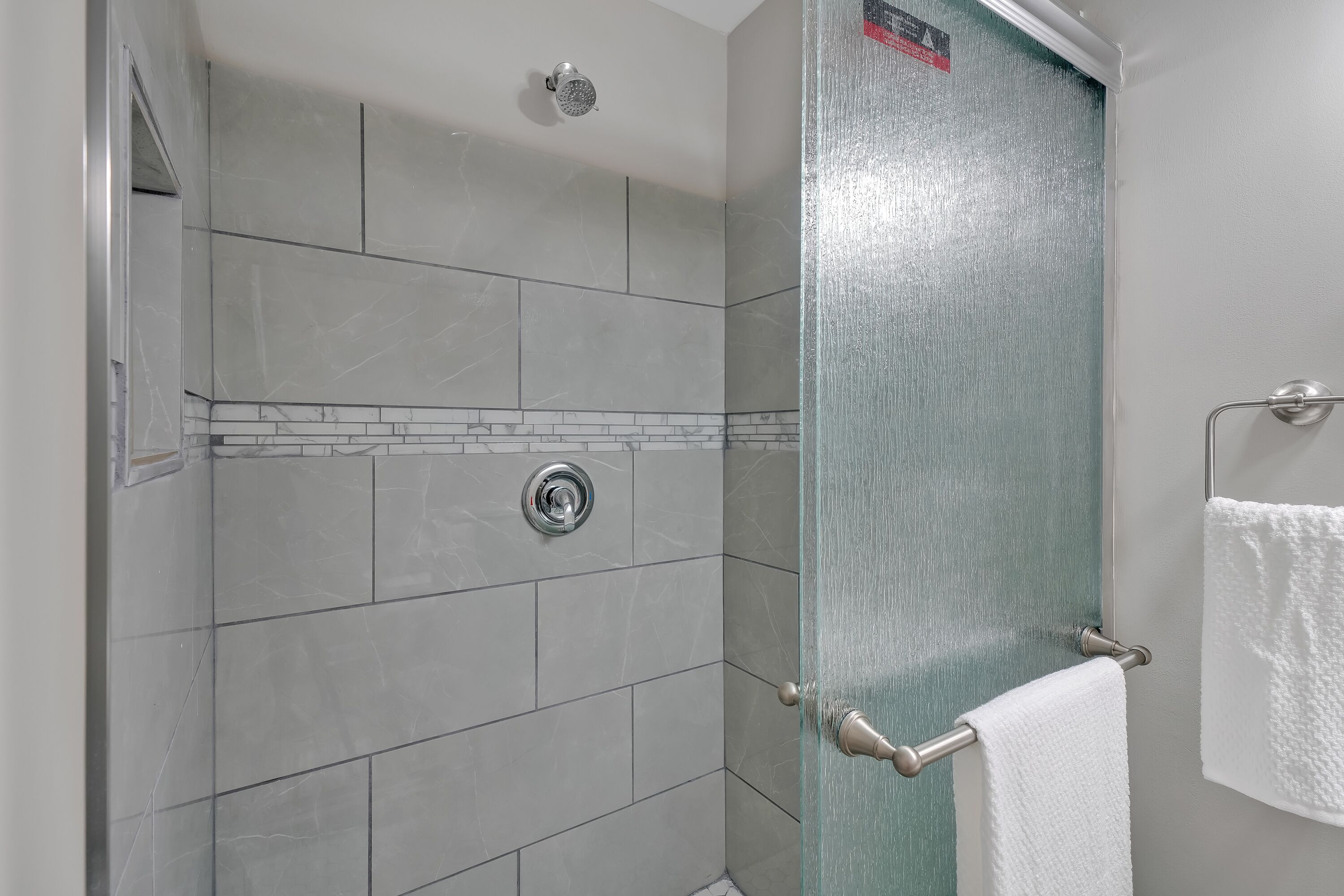 Un espace douche doté d’une porte en verre, d’un porte-serviettes et d’un mur carrelé.