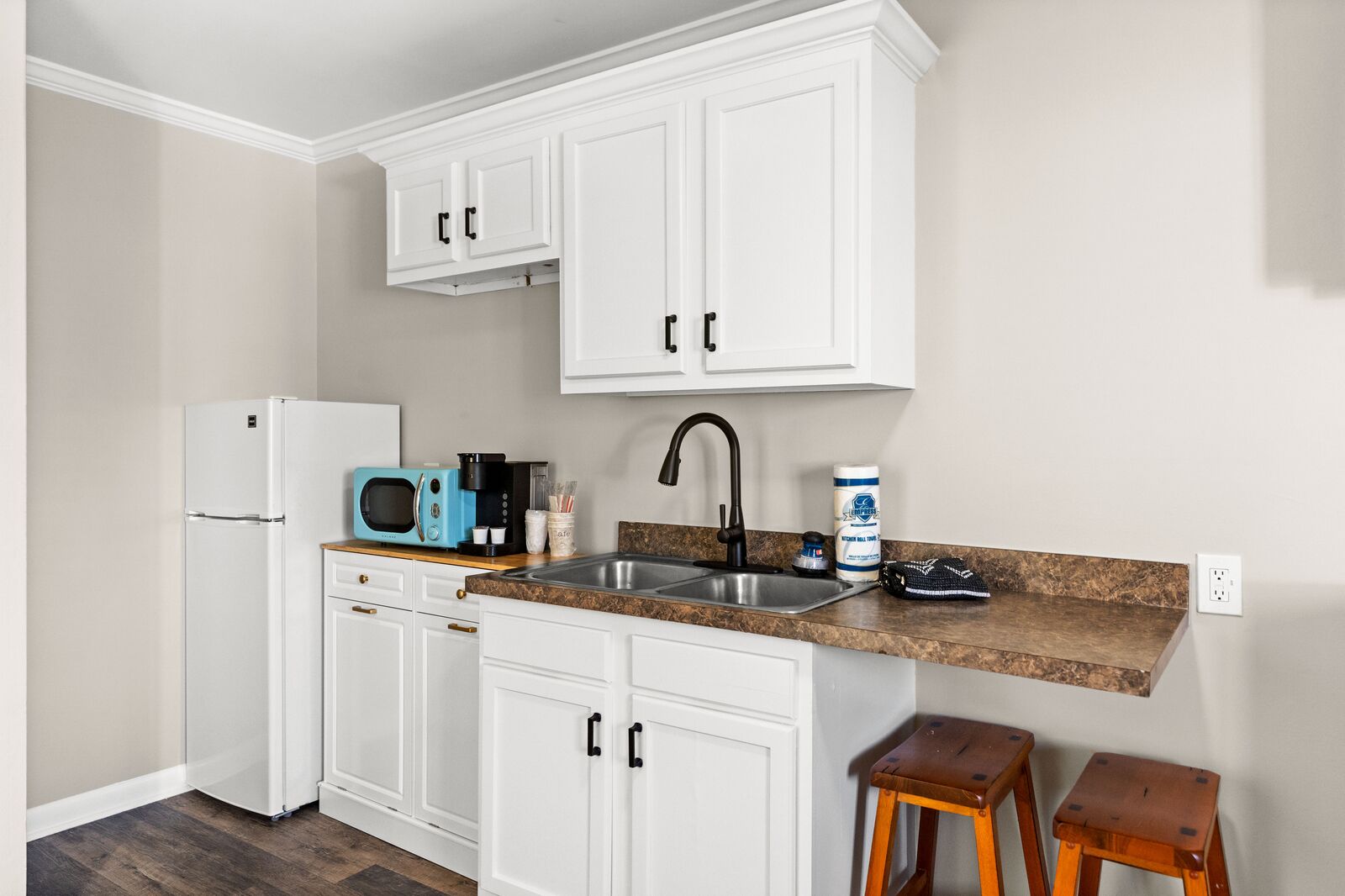 A modern kitchen with white cabinets, a stainless steel sink, a microwave, and a refrigerator.