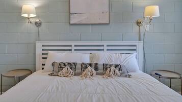 A neatly made bed with white bedding and decorative pillows, two bedside tables with lamps, and a framed artwork on the wall.