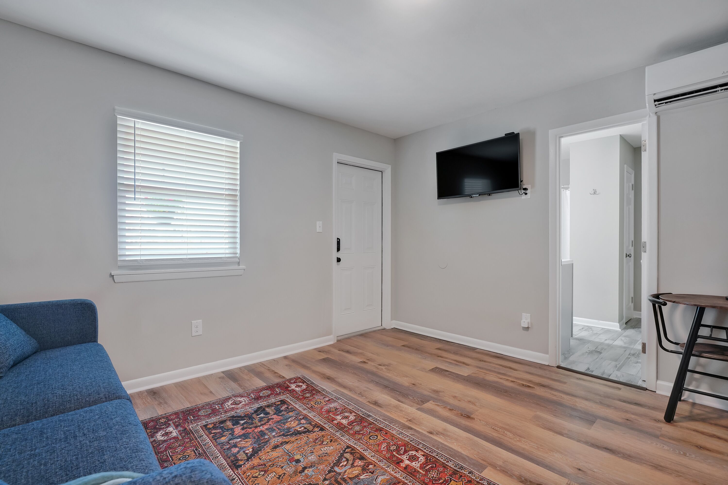 A room with a blue couch, a patterned rug, a flat-screen TV, and a wooden floor.