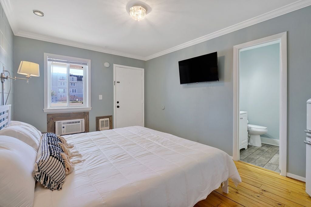 Un dormitorio con cama, televisión, ventana y puerta que da a un baño.