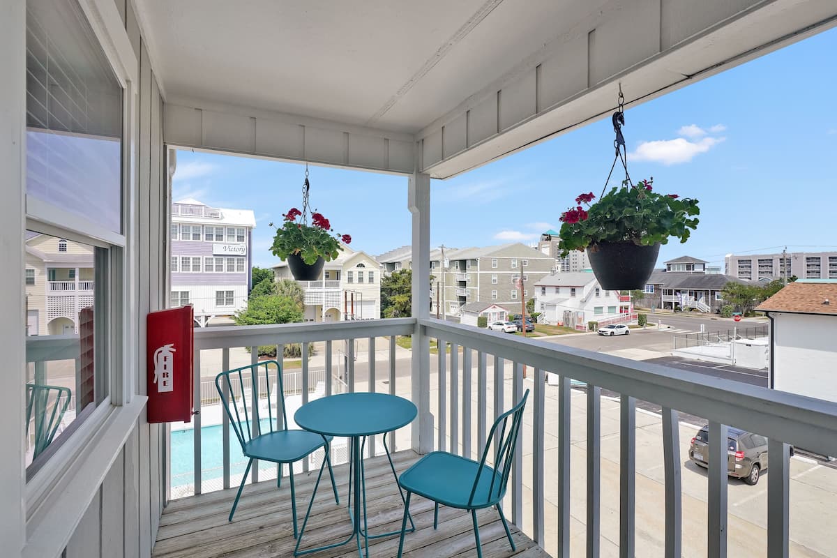 A balcony with two tables and chairs, a hanging flower pot, and a view of a residential area.