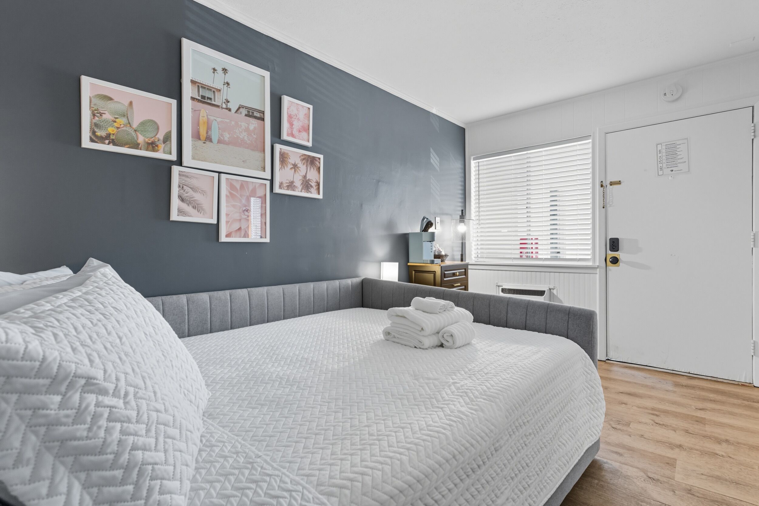 A bedroom with a large bed, a grey headboard, and a wall with framed pictures.