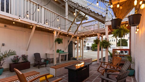 An outdoor patio area with wooden seating, a fire pit, hanging plants, and string lights. - Dry Dock Inn (Carolina Beach)