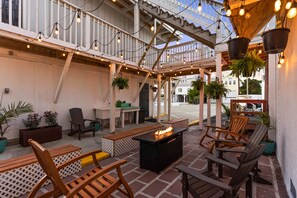An outdoor patio area with wooden seating, a fire pit, hanging plants, and string lights. - Dry Dock Inn (Carolina Beach)