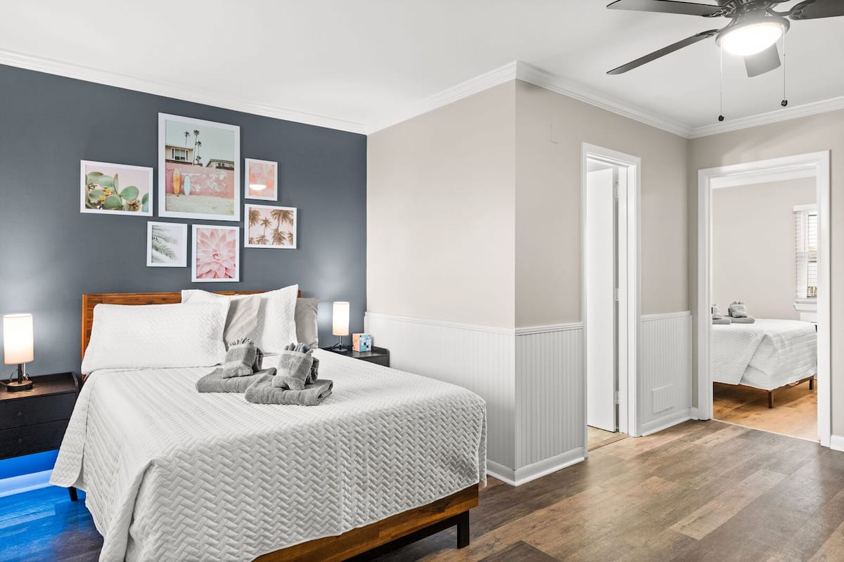 A neatly arranged bedroom with a bed, bedside lamps, and a wall adorned with framed artwork.