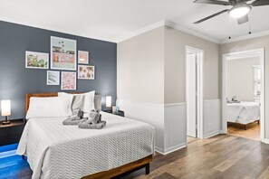 A neatly arranged bedroom with a bed, bedside lamps, and a wall adorned with framed artwork.