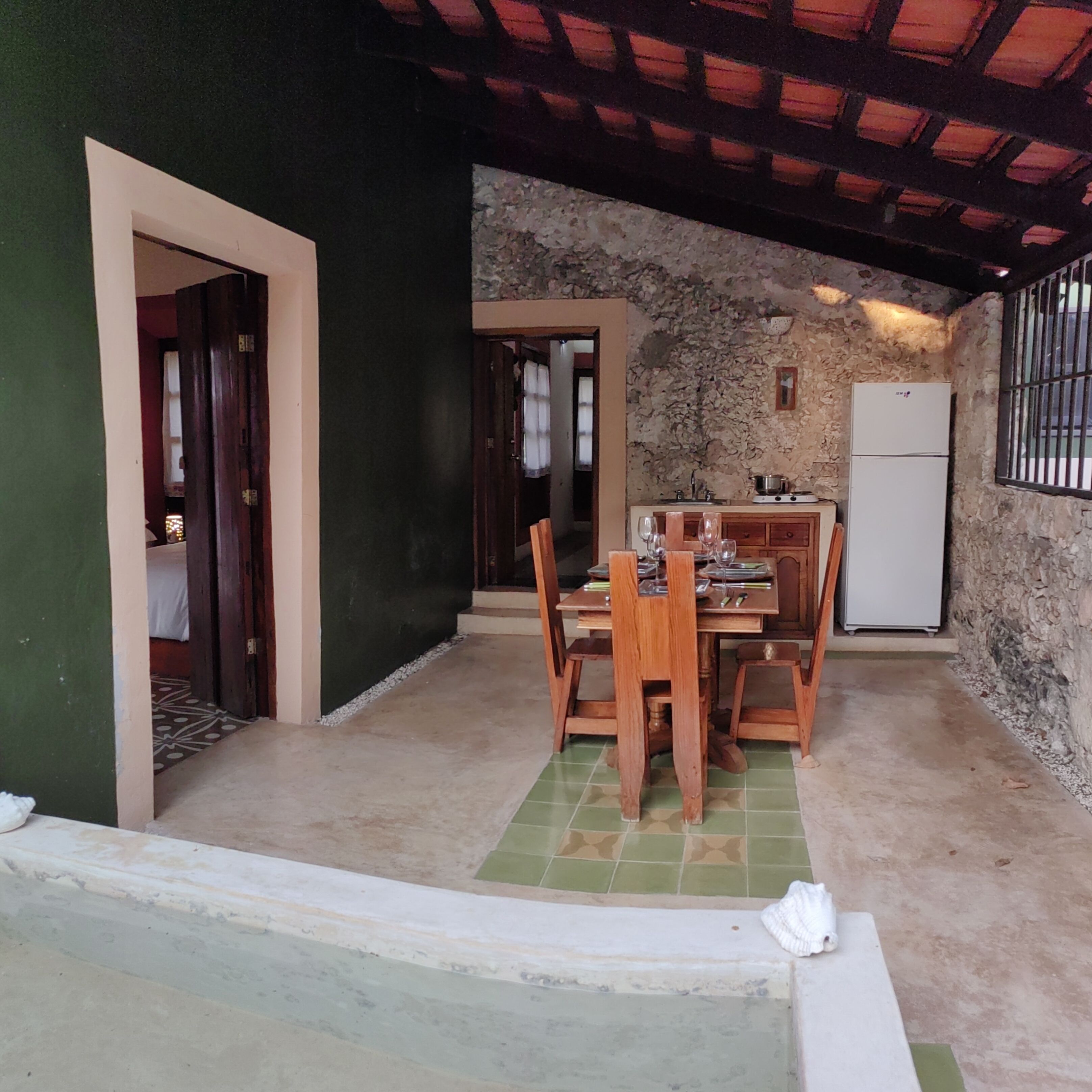 Uma sala de jantar com mesa e cadeiras, uma cozinha com geladeira e uma parede de pedra.