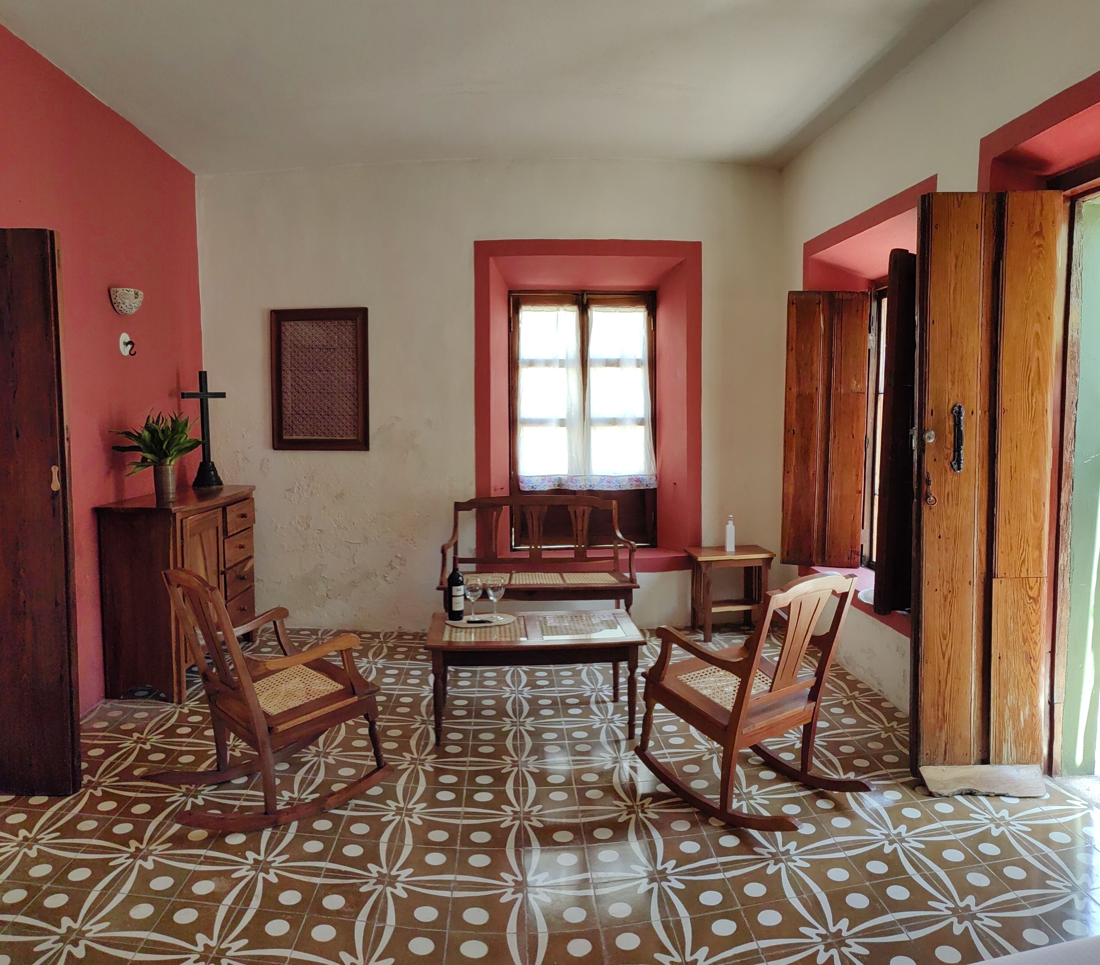 Una habitación con suelo de baldosas, muebles de madera, una ventana con cortinas y una puerta.