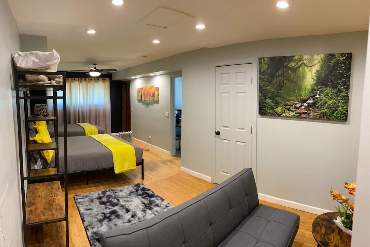 A modern bedroom with bunk beds, a grey sofa, a wooden floor, and a forest-themed wall art.