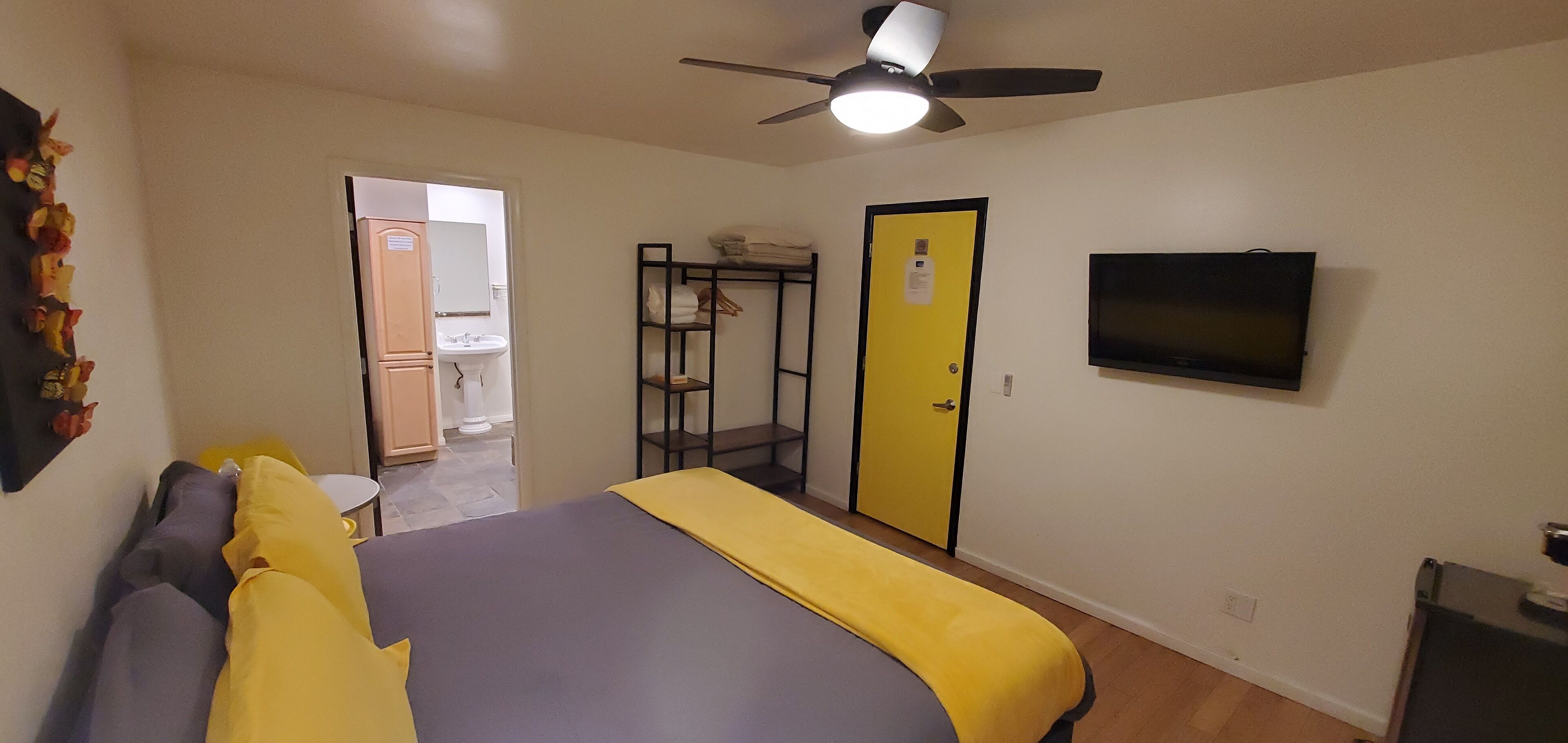 A bedroom with a bed, a ceiling fan, a TV, a wardrobe, and a bathroom visible through an open door.