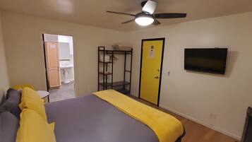 A bedroom with a bed, a ceiling fan, a TV, a wardrobe, and a bathroom visible through an open door.