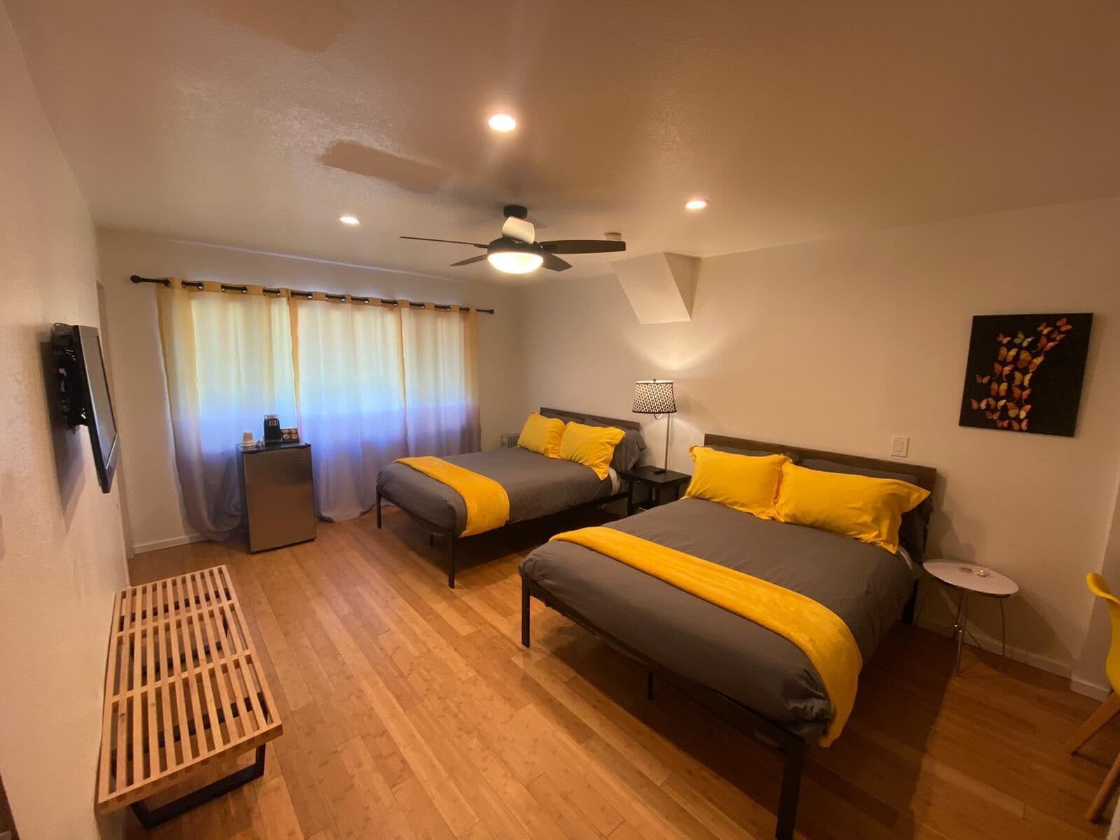 A hotel room with two beds, a ceiling fan, a desk, a chair, and a painting on the wall.