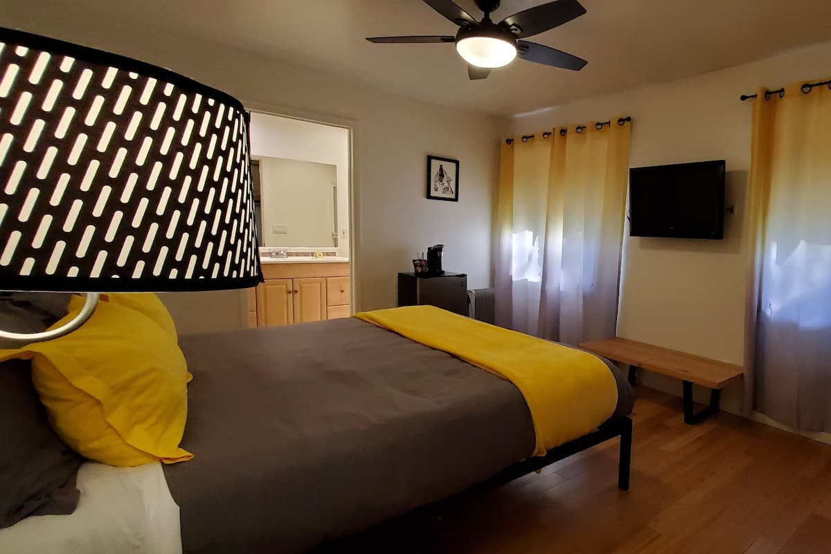 A bedroom with a bed, a bedside table, a lamp, a TV, and curtains.