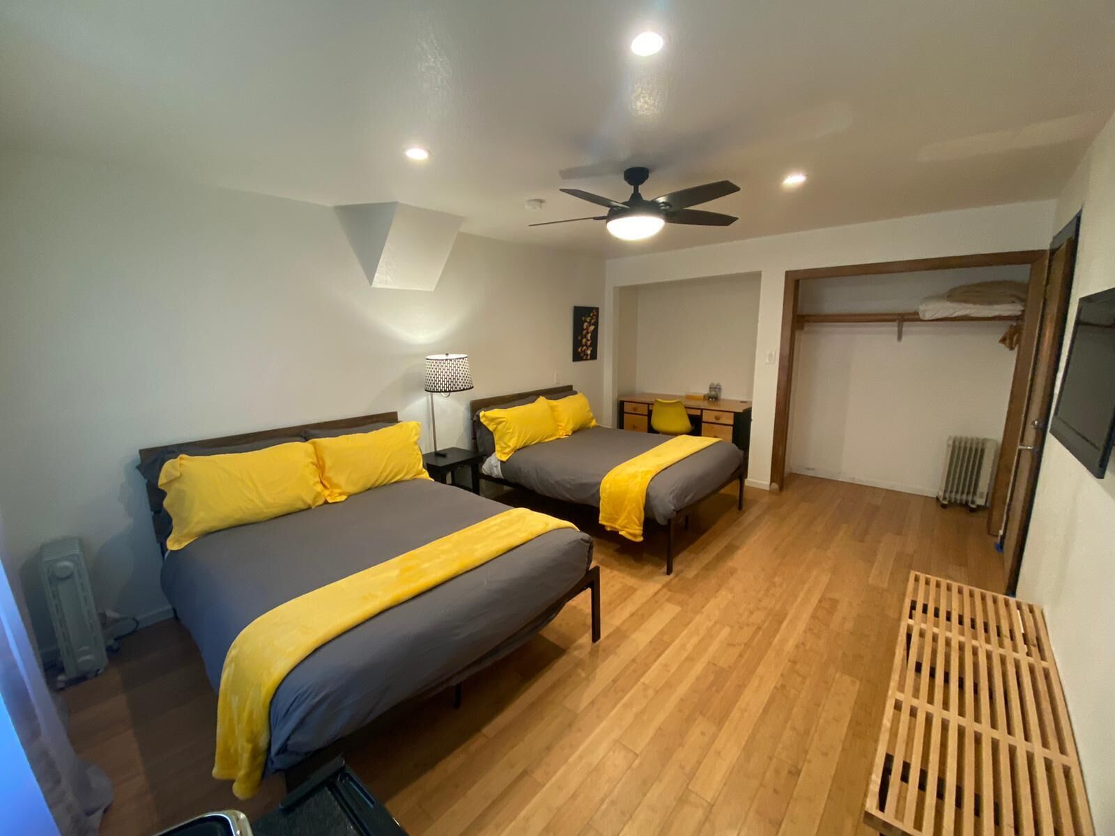 A bedroom with two beds, a ceiling fan, a desk, and a radiator.