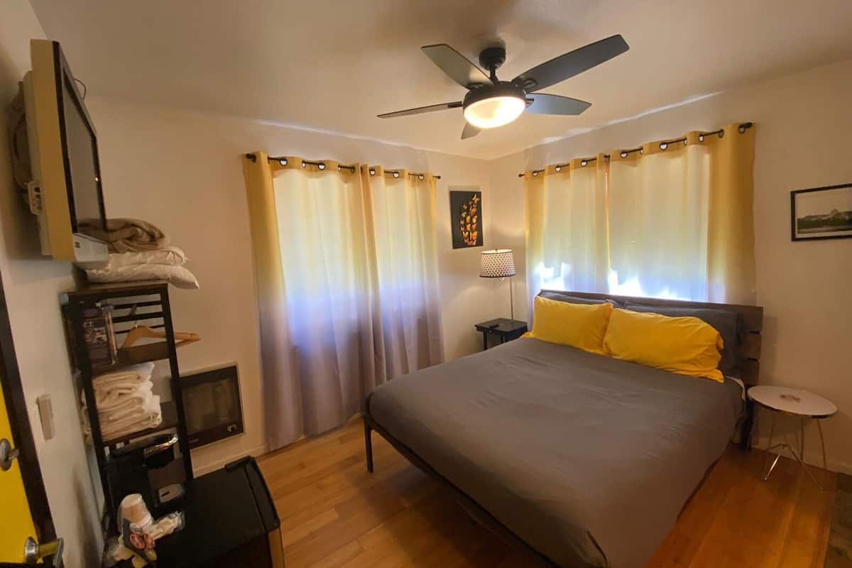 A bedroom with a bed, a ceiling fan, a bedside table, a lamp, and a shelf with towels.