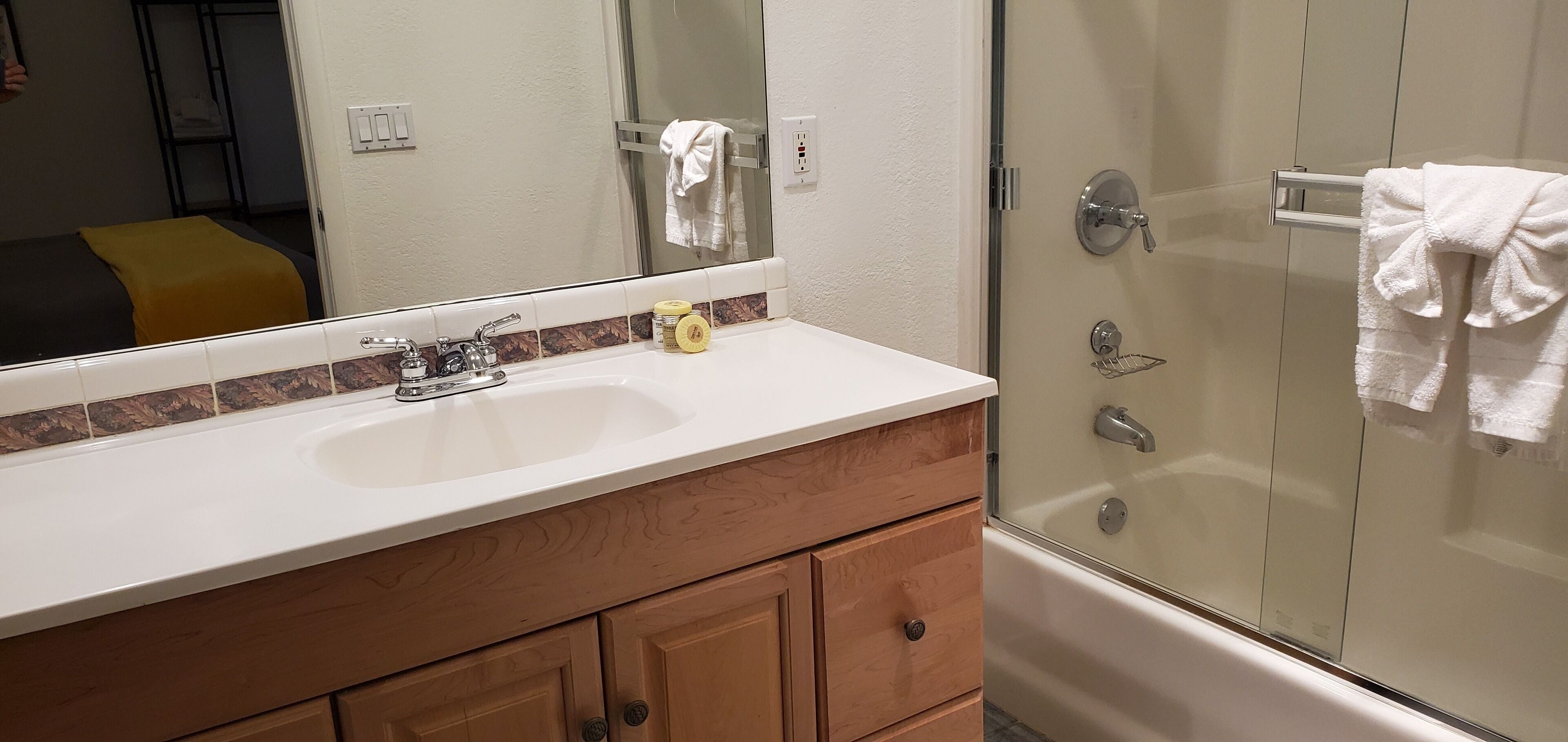 A bathroom with a white sink, wooden vanity, and a glass shower enclosure.