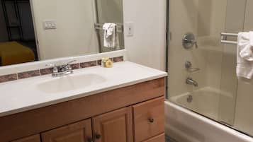 A bathroom with a white sink, wooden vanity, and a glass shower enclosure.