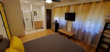 Un dormitorio con cama, una banca, televisión, ducha y baño.