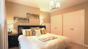 Un dormitorio con una cama, mesitas de noche, una lámpara, una luz de techo y dos puertas.
