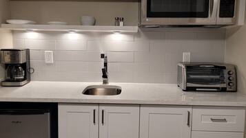 A modern kitchen with white cabinets, a stainless steel sink, a microwave, a toaster, and a dishwasher.