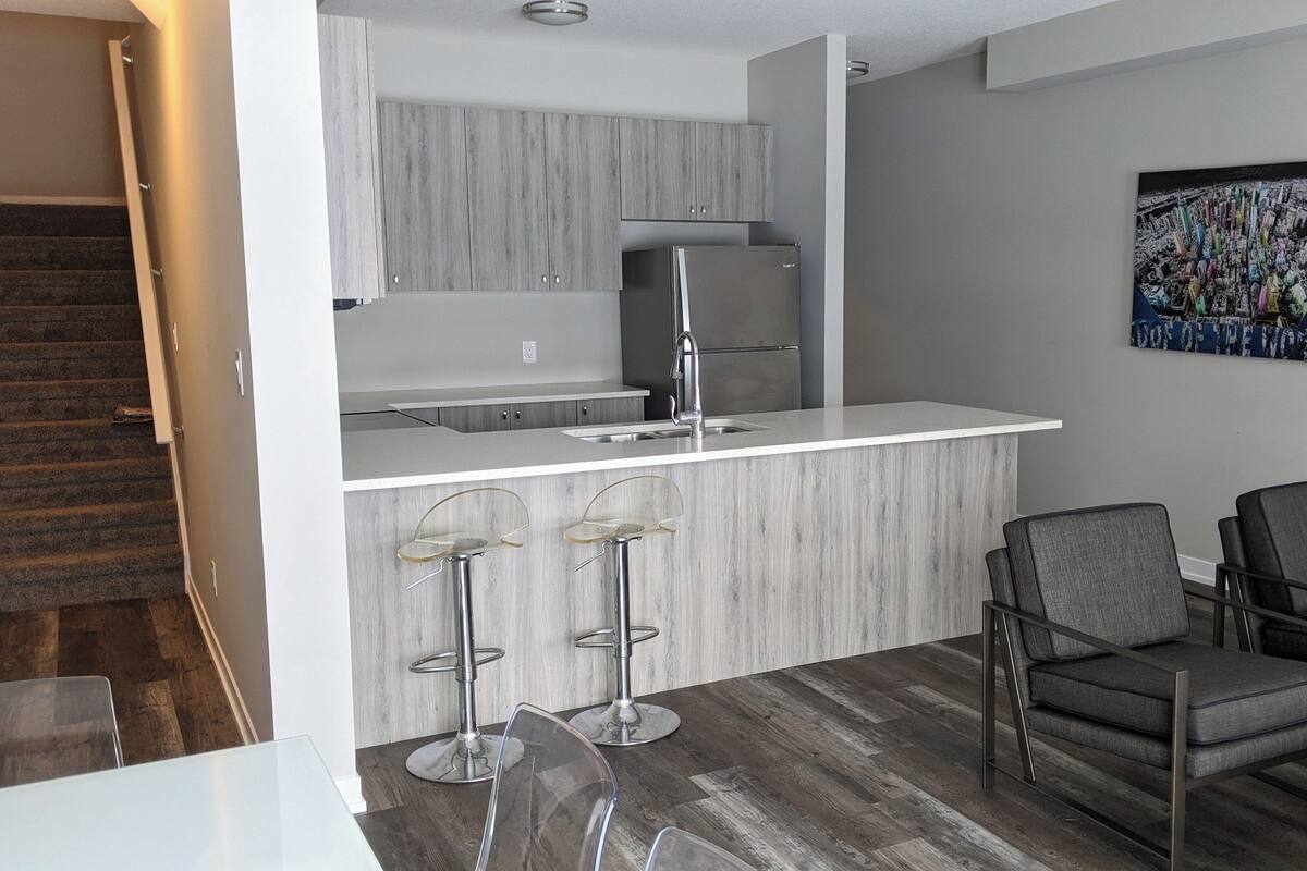 A modern kitchen with a built-in refrigerator, a bar area with stools, and a dining table with chairs.