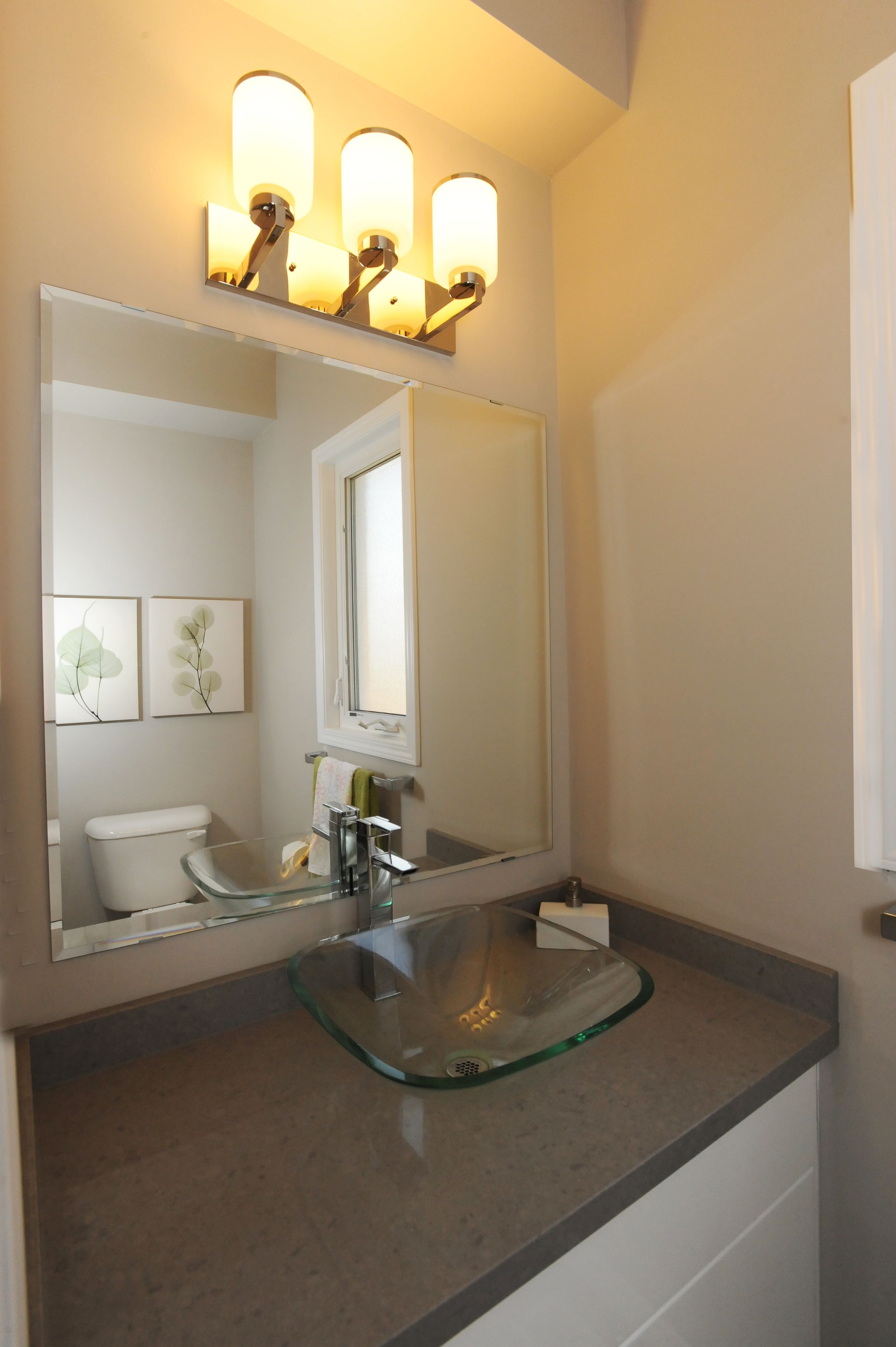 Un baño con un lavabo de vidrio, un espejo e iluminación en la pared.