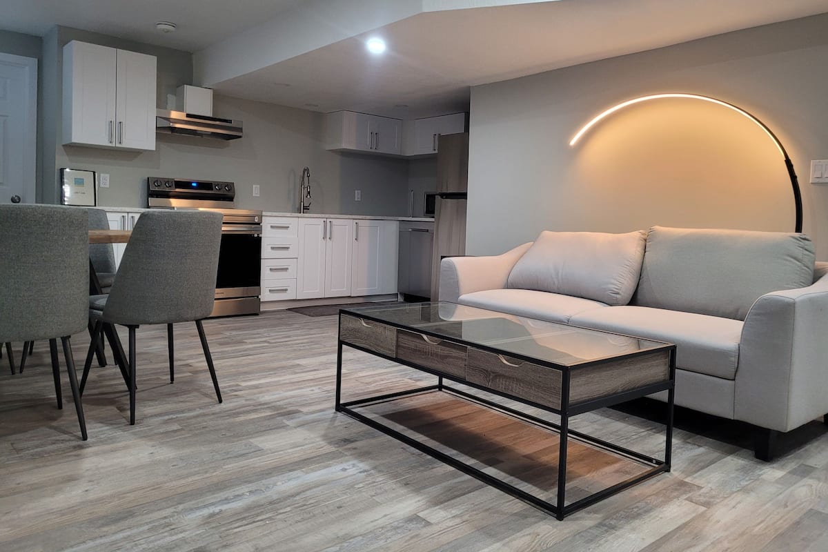 A modern living room with a glass coffee table, grey sofa, and a dining area with chairs.