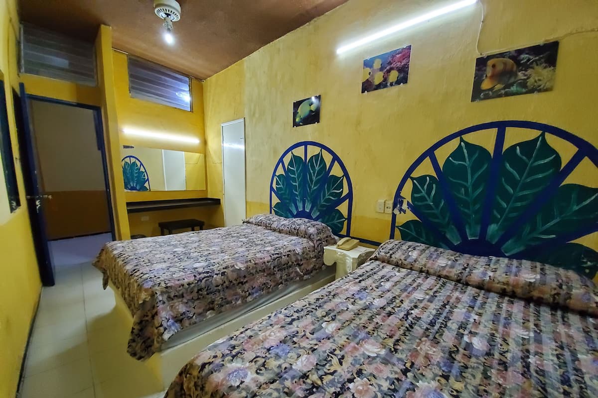 A room with two beds, a desk, and a chair. There are two wall-mounted light fixtures and a ceiling fan.