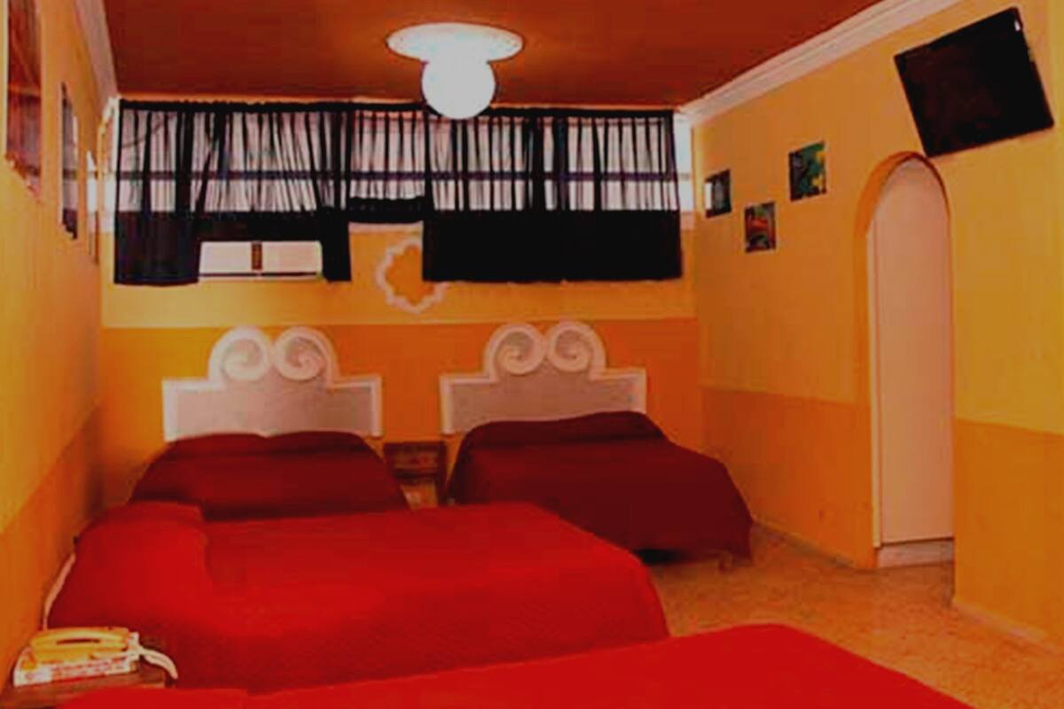 A room with two beds, a white ceiling light, a window with black curtains, and a door with a white frame.