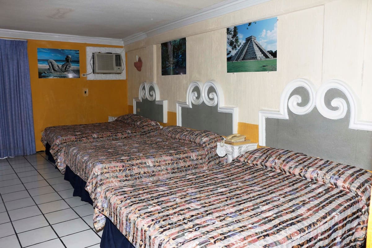 A hotel room with two beds, a tiled floor, and wall decorations including a painting of a pyramid and a waterfall.