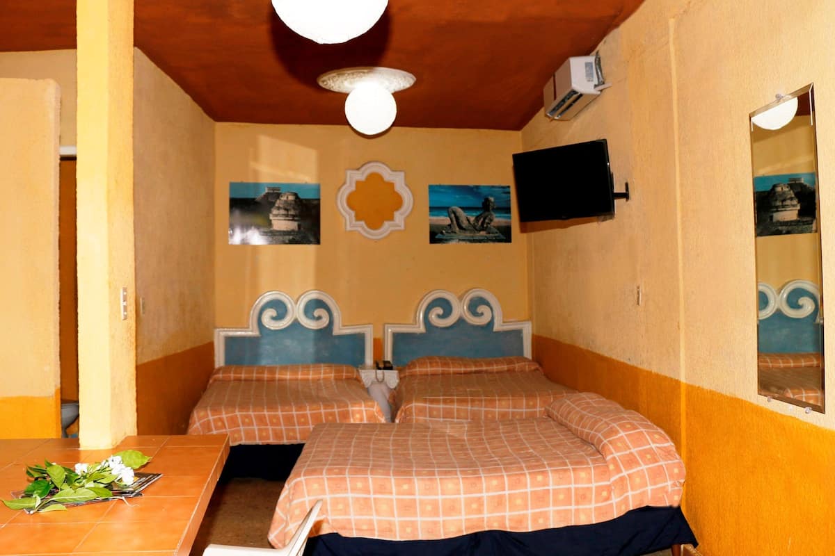 A room with two beds, a table with a flower arrangement, and a wall-mounted TV.