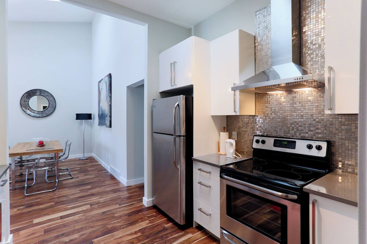Una cocina moderna con electrodomésticos de acero inoxidable, armarios blancos y una salpicadura de azulejos.