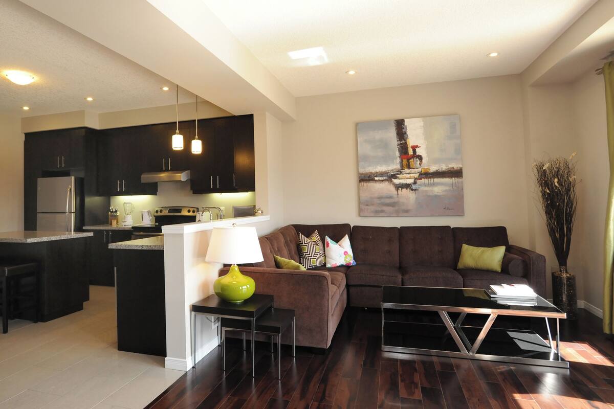 Una sala de estar moderna con sofá, mesa de centro y zona de cocina con armarios oscuros y refrigerador.