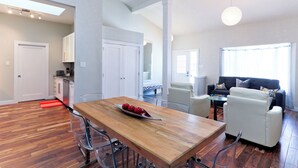 Un vaste espace de vie comprenant une table à manger en bois, des canapés blancs et une cuisine à l’arrière-plan.