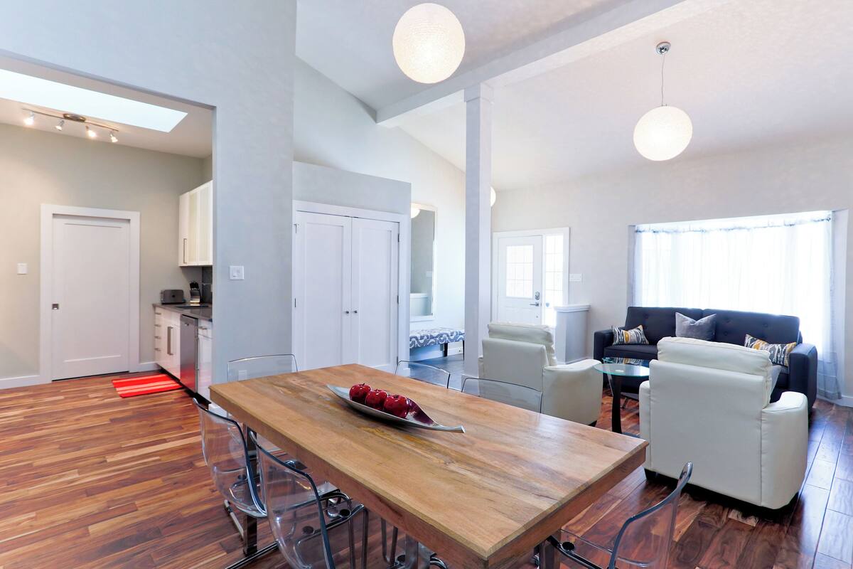 Un salón amplio con una mesa de comedor de madera, sofás blancos y una cocina al fondo.