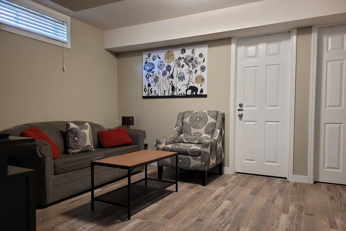 Una sala de estar con un sofá gris, cojines estampados en rojo y negro, un sillón estampado, una mesa de centro de madera y una obra de arte floral colgada en la pared.