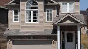 Une maison à deux étages avec un garage, un porche à l’avant et une façade symétrique.