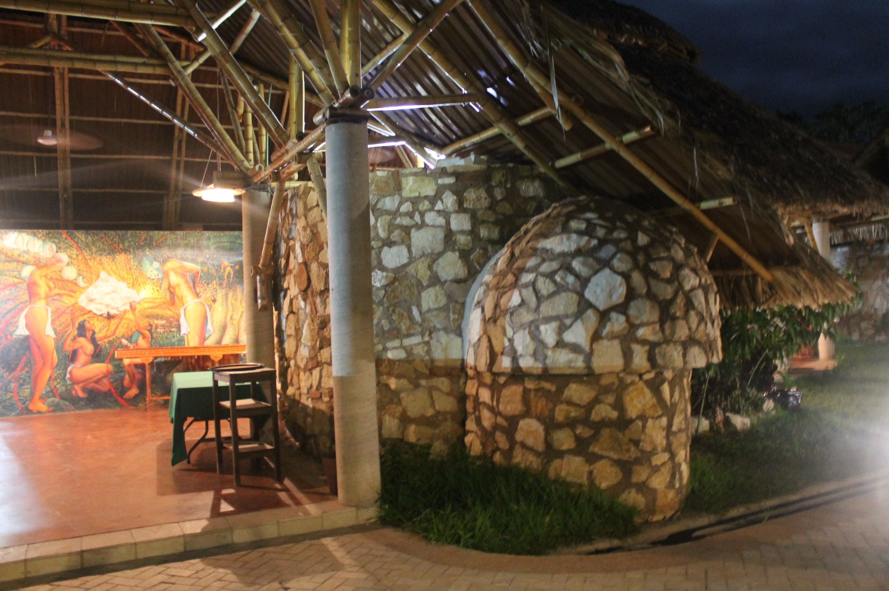 Una estructura de piedra con techo de paja, un mural en la pared y una mesa con sillas.