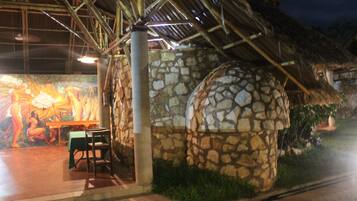 Una estructura de piedra con techo de paja, un mural en la pared y una mesa con sillas.
