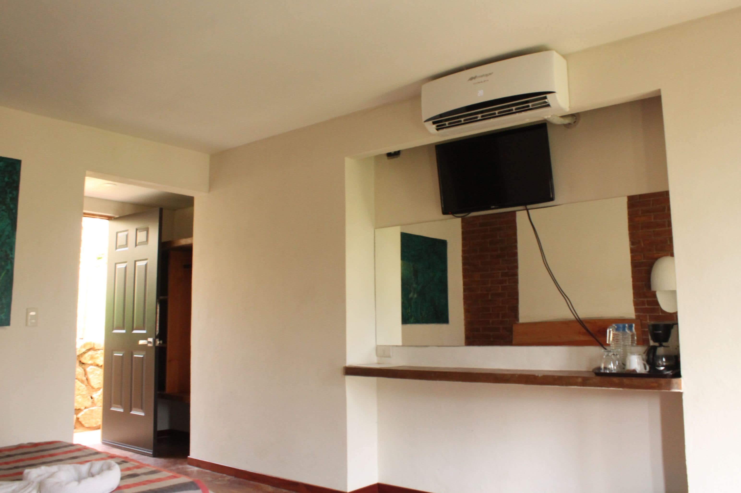 A hotel room with a bed, a mounted television, a coffee maker, and an air conditioning unit.