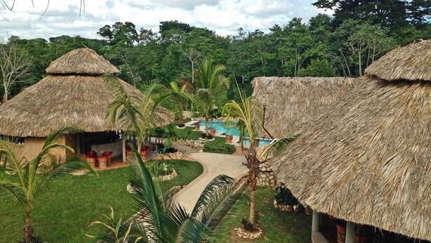 Un resort con cabañas de techo de paja, una piscina y un jardín bien cuidado.