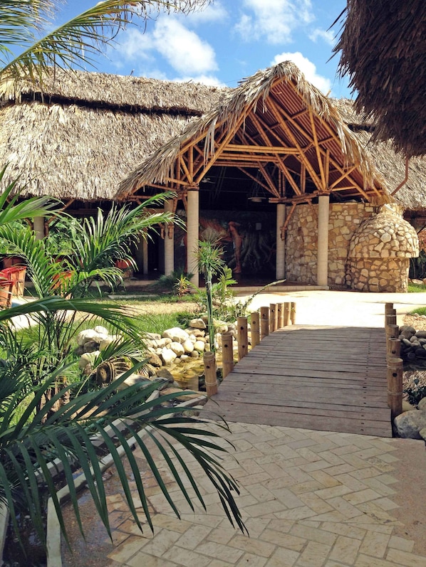 A thatched-roof structure with a stone wall, a wooden deck, and tropical plants.